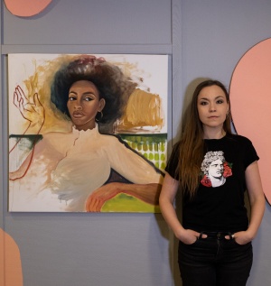 Konstrundan, Konsten fredag, bild på konstnär Anna Semerdjiev. Anna står bredvid en målning av en mörkhyad kvinna me afrofrisyr.