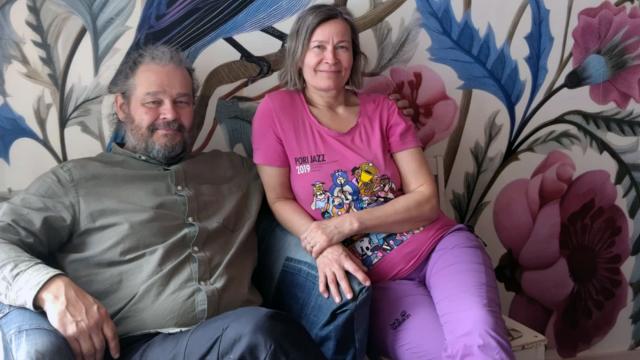 Pasi och Virpi sitter i en soffa tillsammans och ler mot kameran.