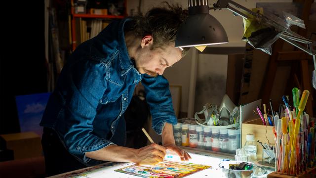 Alexander står böjd över sitt skrivbord och målar i sin ateljé.